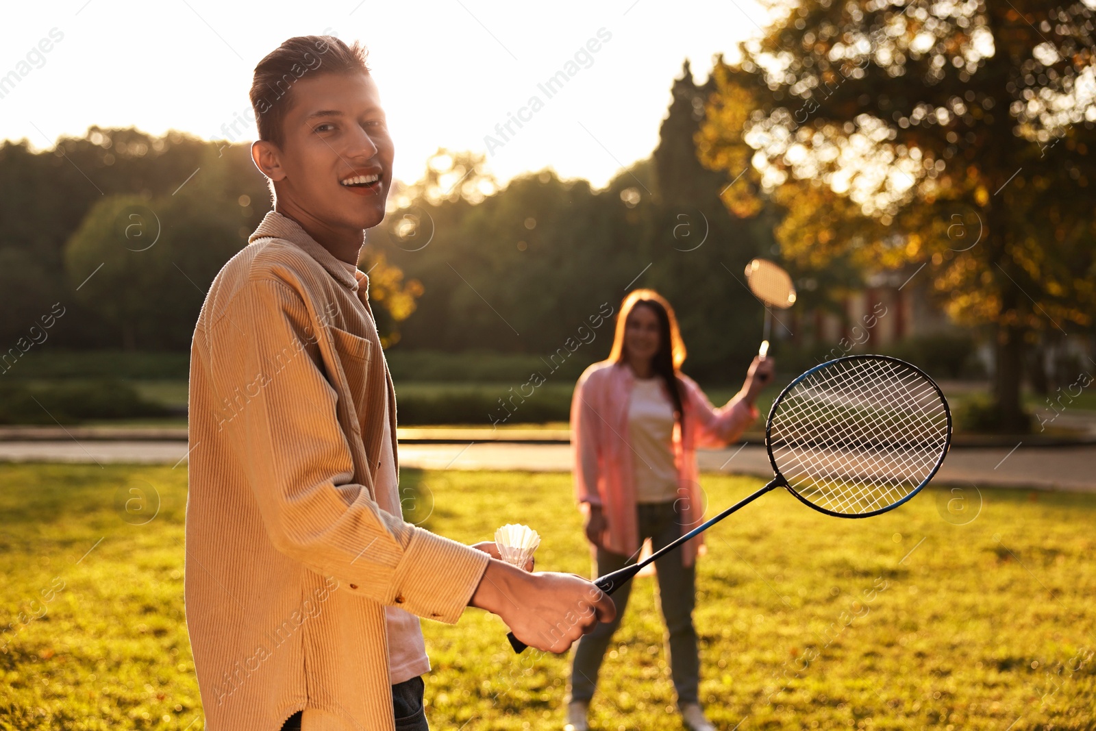 Photo of Young man and woman playing badminton in park on sunny day, selective focus