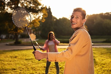 Photo of Young man and woman playing badminton in park on sunny day, selective focus