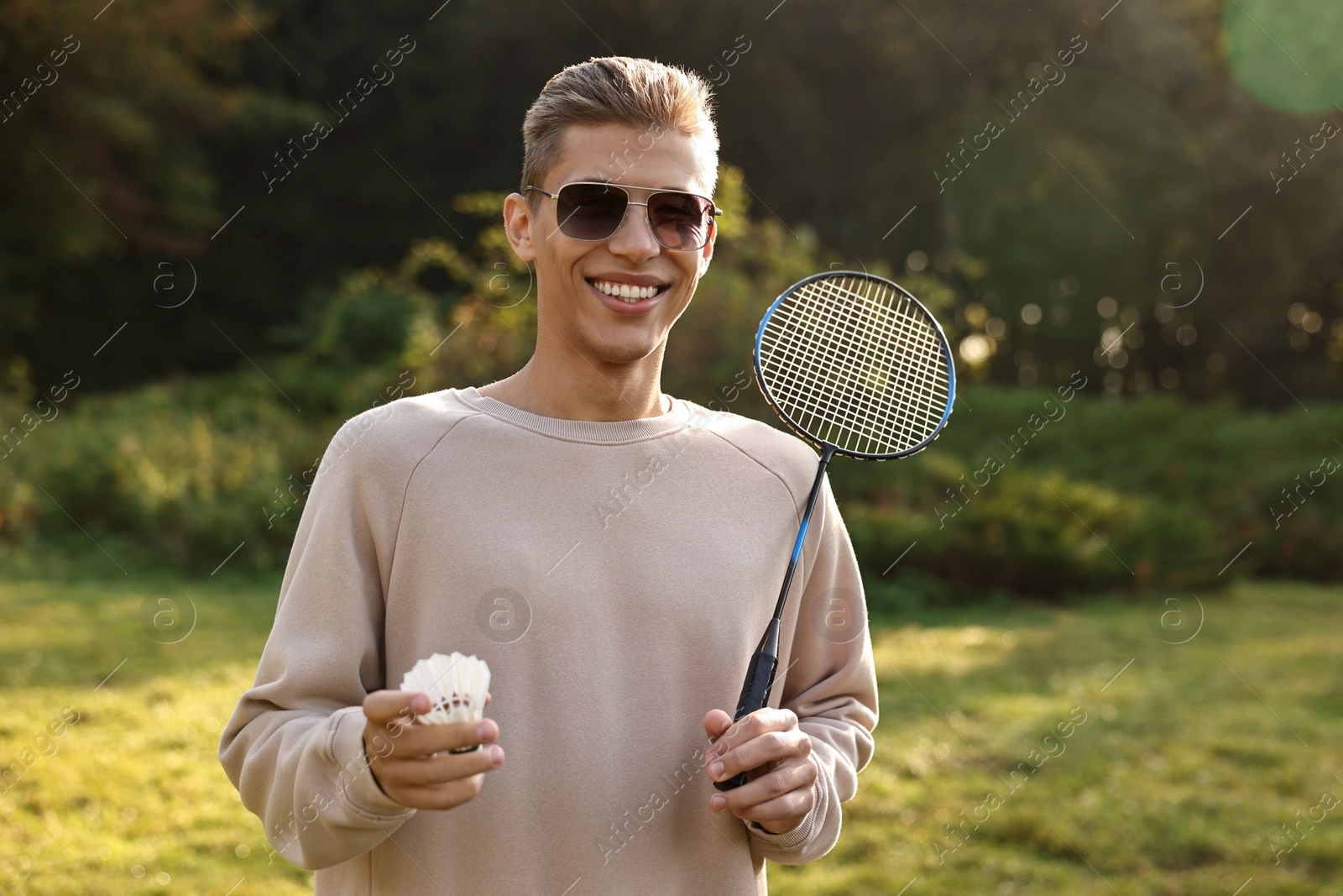 Photo of Happy young man with badminton racket and shuttlecock in park on sunny day