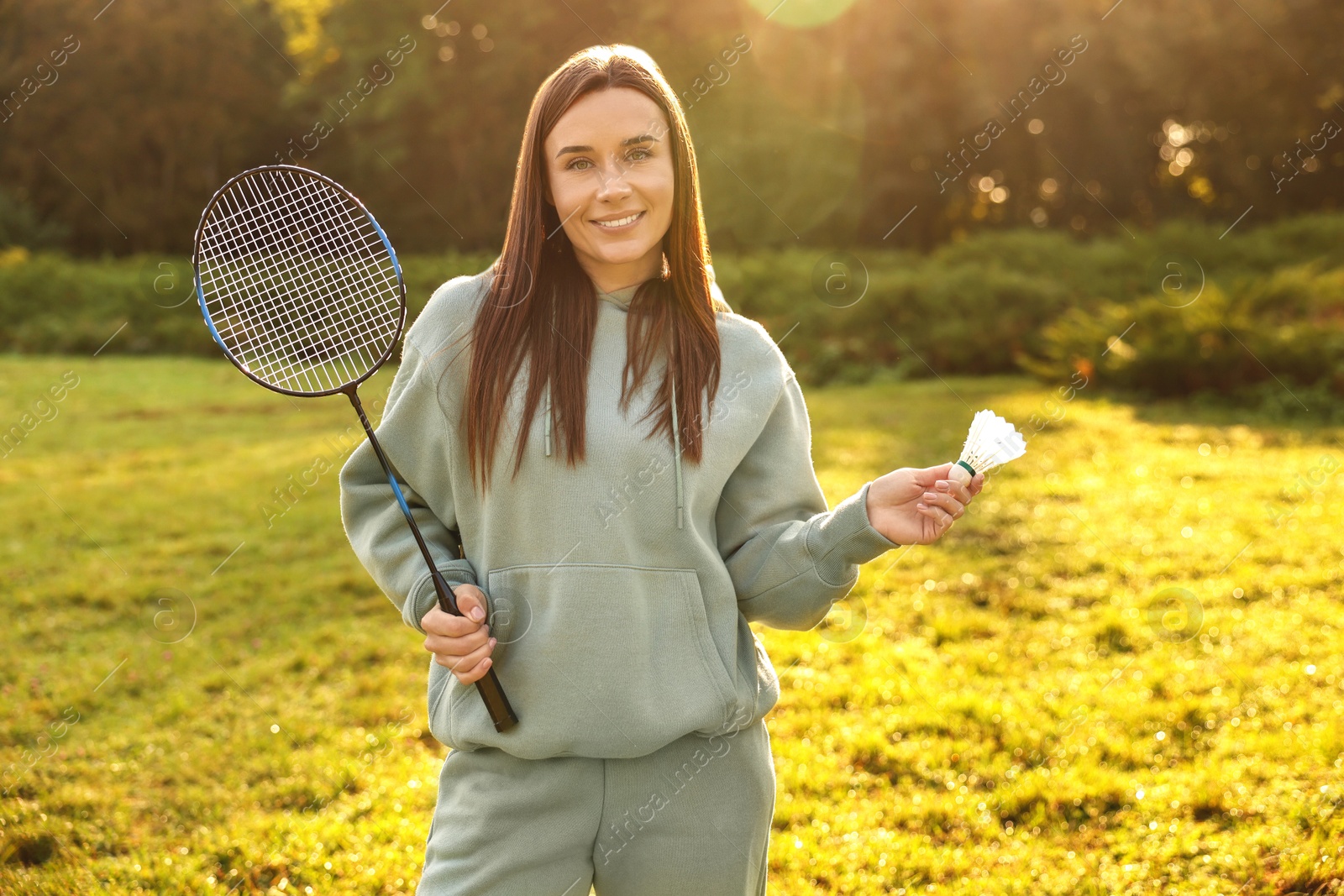 Photo of Happy young woman with badminton racket and shuttlecock in park on sunny day