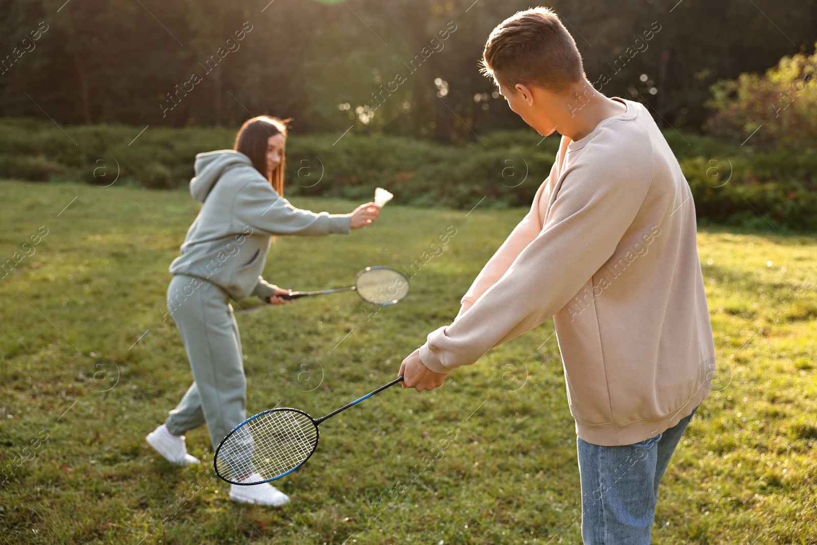 Photo of Young woman and man playing badminton in park on sunny day, selective focus