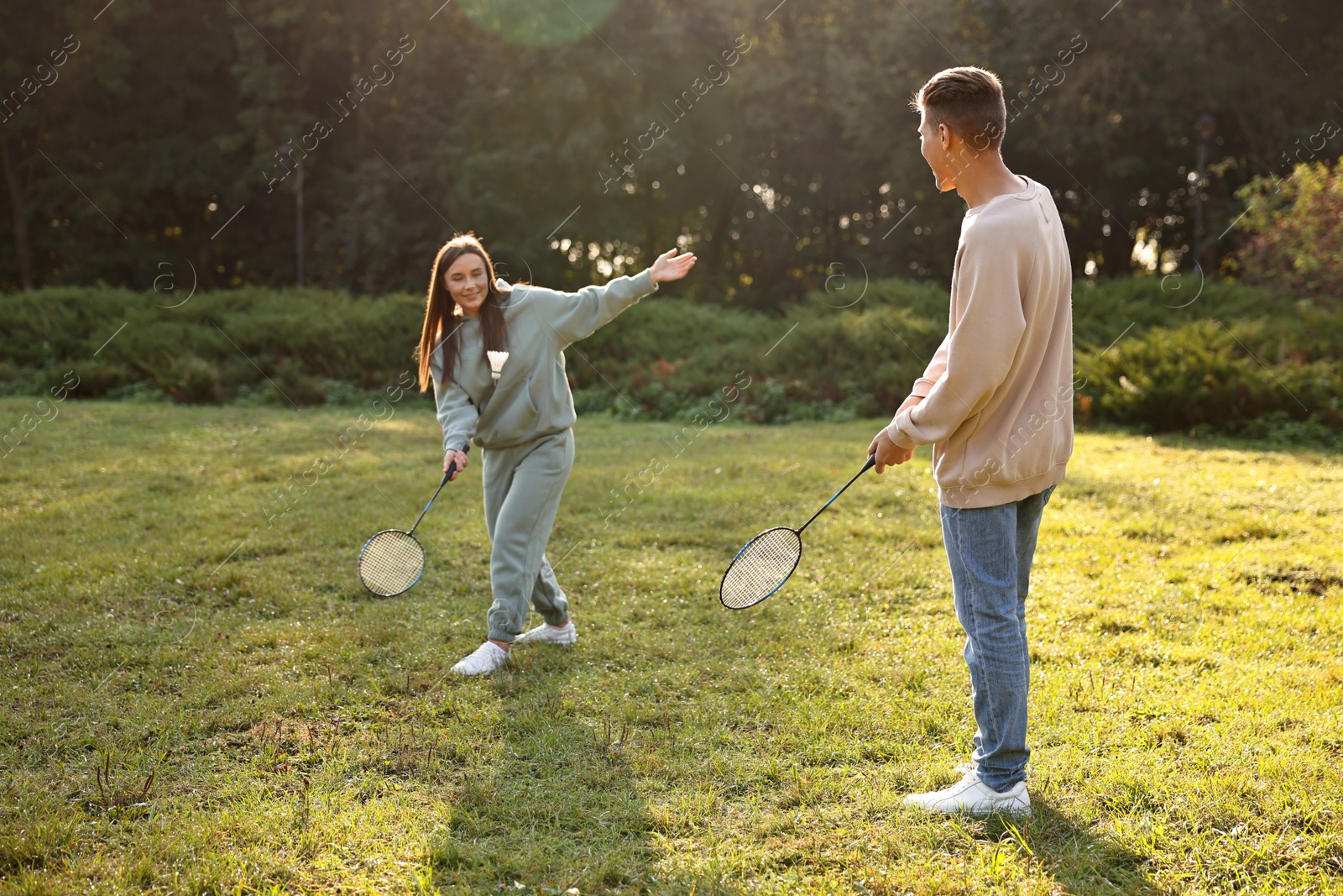 Photo of Young woman and man playing badminton in park on sunny day, selective focus