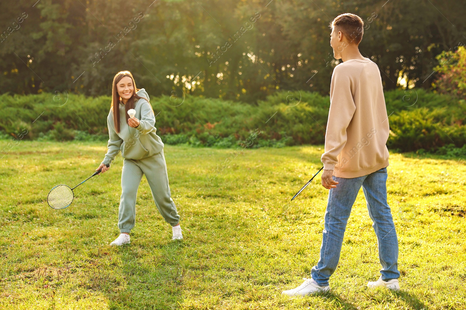 Photo of Young woman and man playing badminton in park on sunny day, selective focus