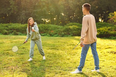 Photo of Young woman and man playing badminton in park on sunny day, selective focus