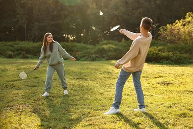 Photo of Young woman and man playing badminton in park on sunny day, selective focus