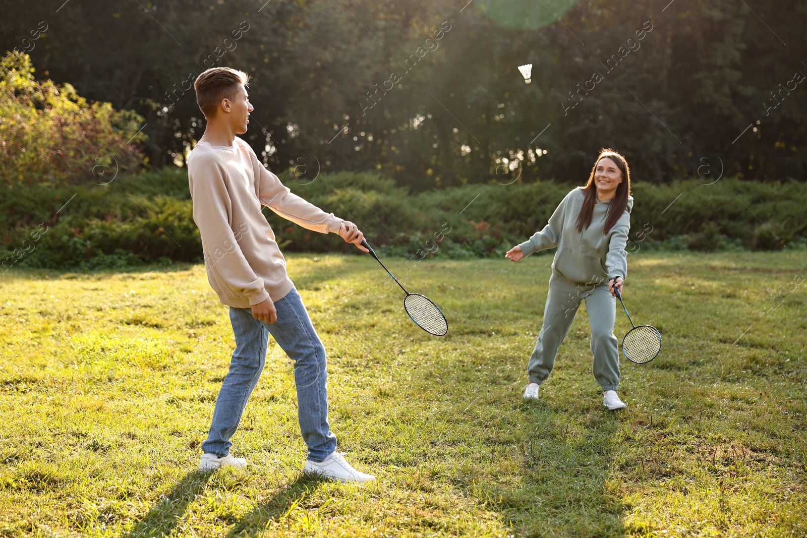 Photo of Young woman and man playing badminton in park on sunny day, selective focus