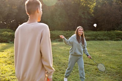 Photo of Young woman and man playing badminton in park on sunny day, selective focus