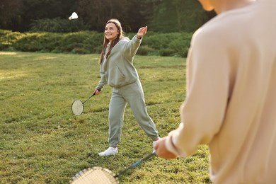 Photo of Young woman and man playing badminton in park on sunny day, selective focus