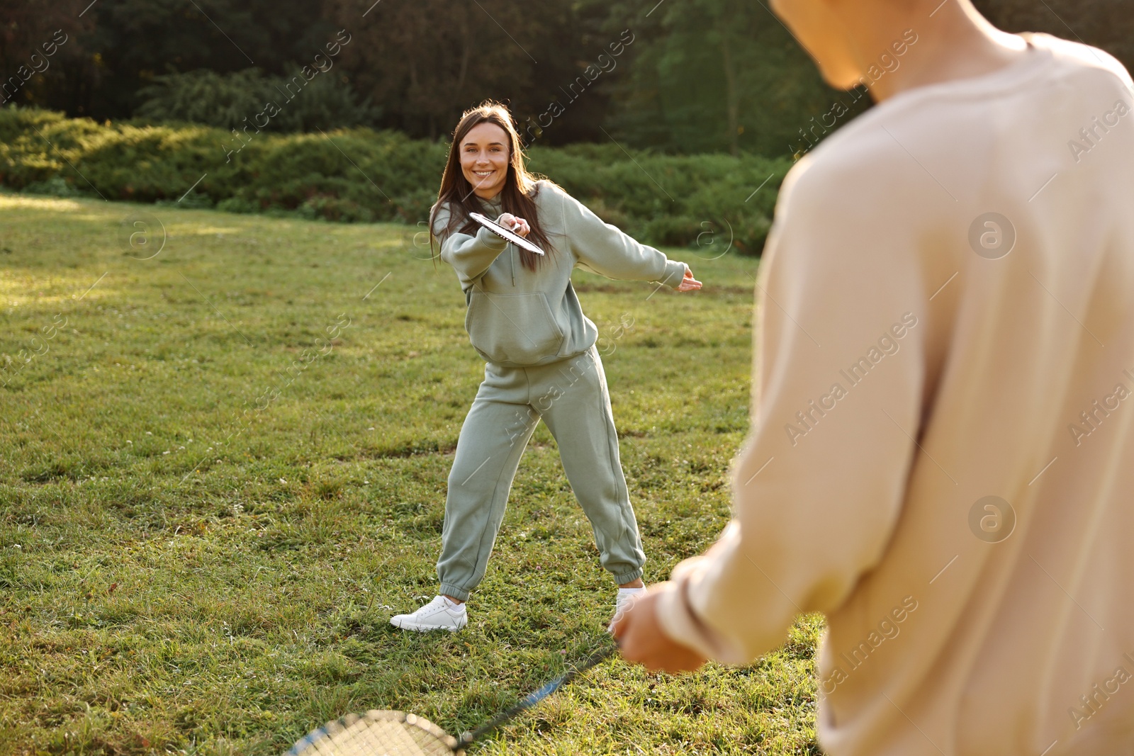 Photo of Young woman and man playing badminton in park on sunny day, selective focus