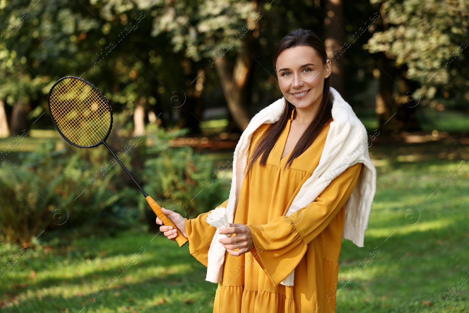 Photo of Happy young woman with badminton racket and shuttlecock in park