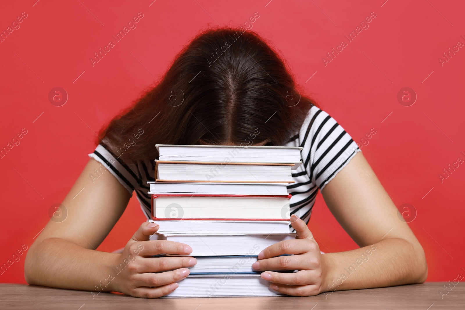 Photo of Young student with stack of books having stress before exam at table against red background