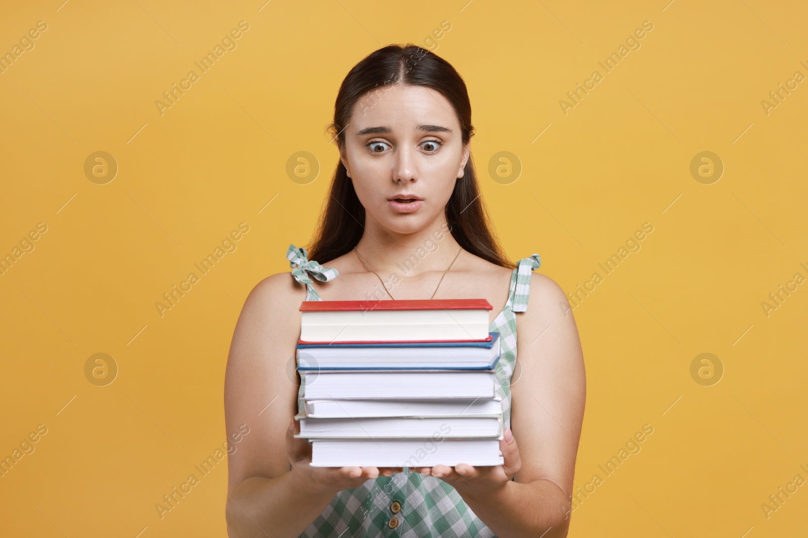 Photo of Stressful student with stack of books before exam on orange background