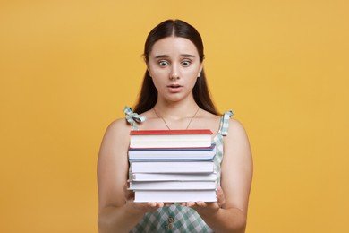 Photo of Stressful student with stack of books before exam on orange background