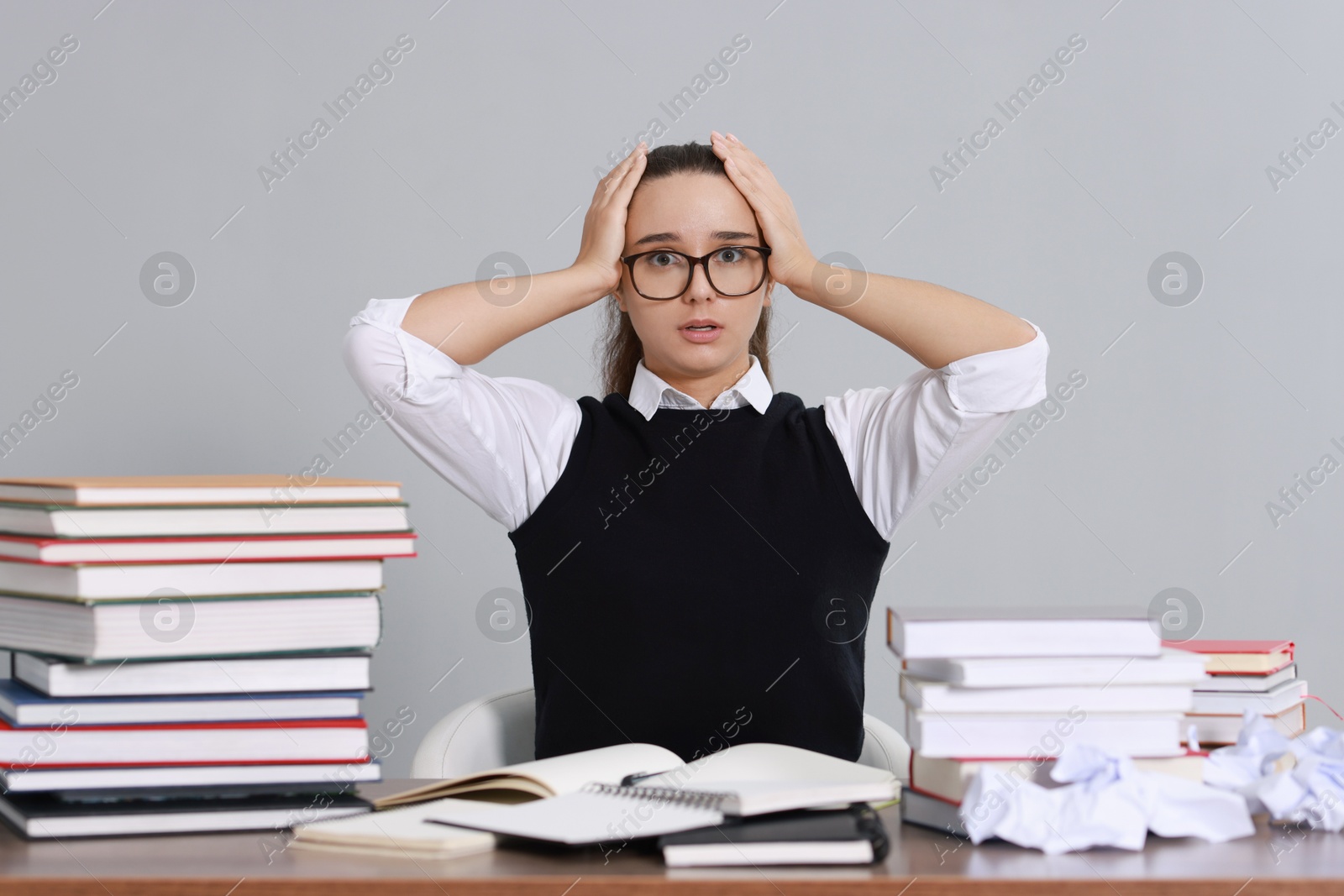 Photo of Young student having stress before exam at desk against grey background