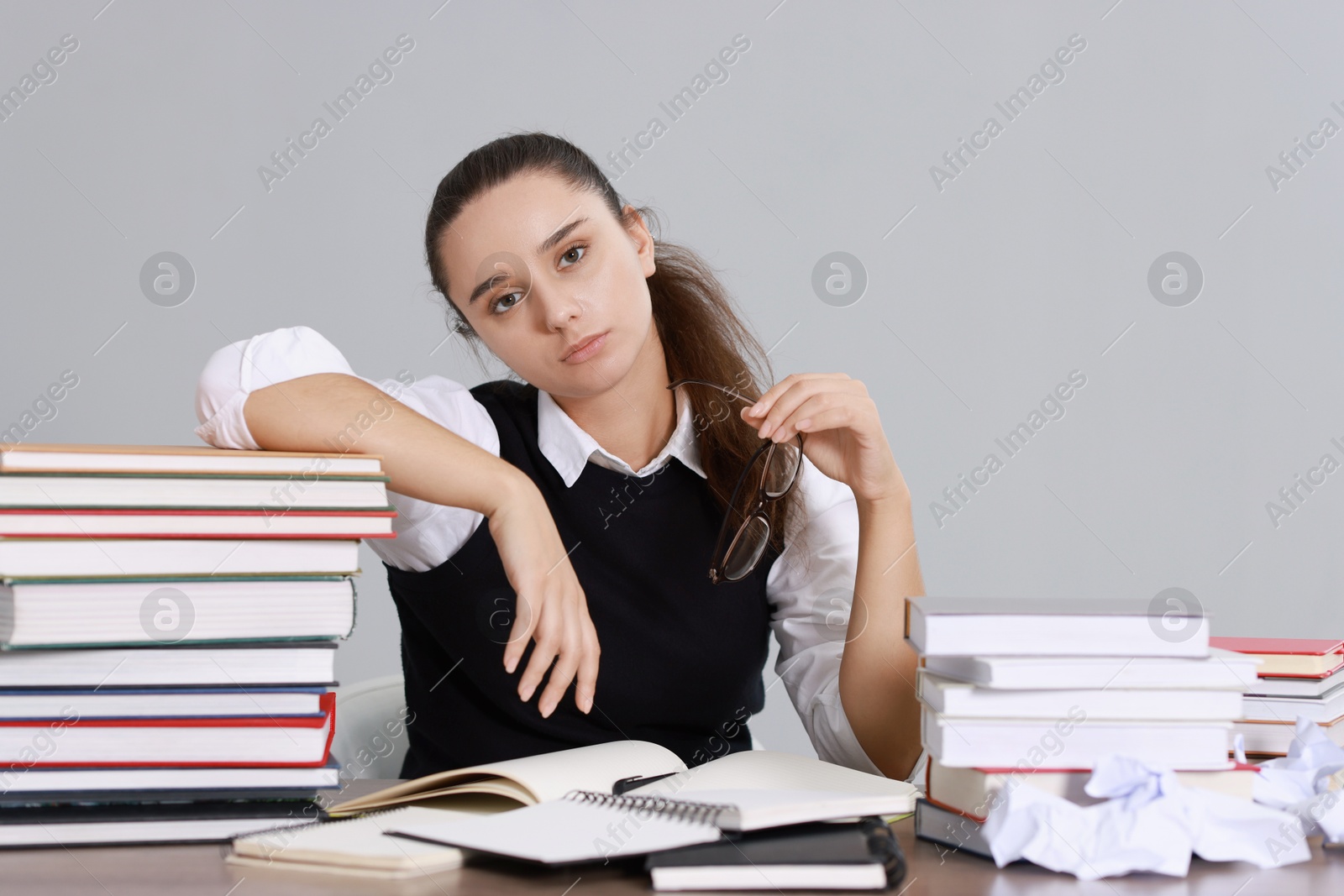 Photo of Young student having stress before exam at desk against grey background