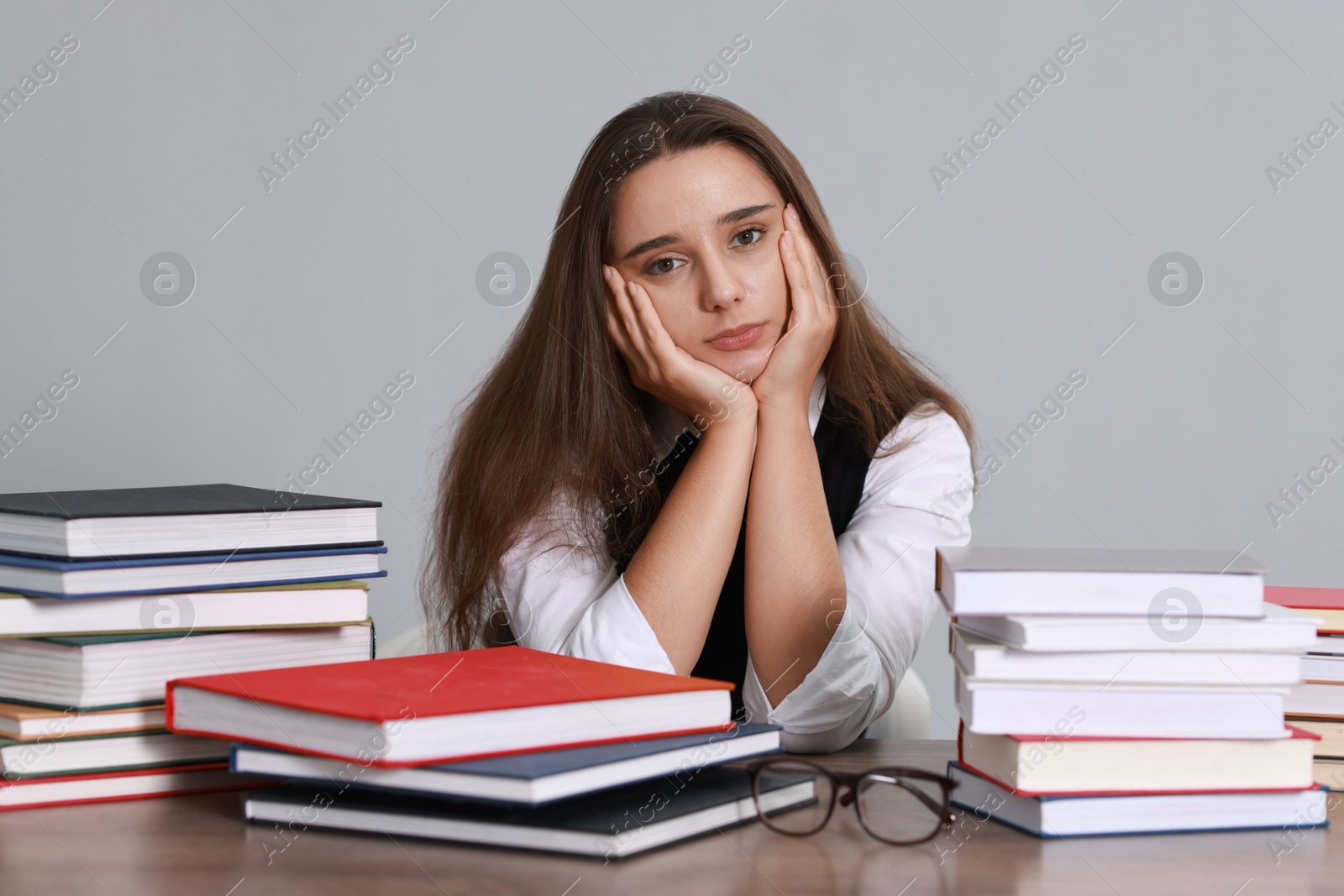 Photo of Young student having stress before exam at desk against grey background