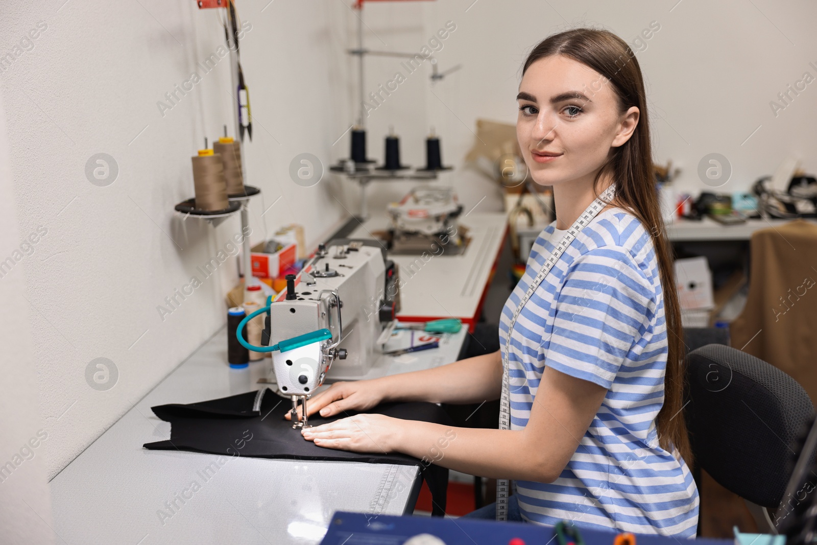 Photo of Young woman working with sewing machine in professional workshop