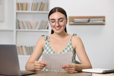 Photo of Happy student reading her good exam result at table indoors