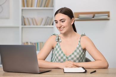 Student feeling happy about her good exam result at table with laptop indoors