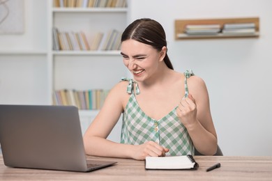 Photo of Student feeling happy about her good exam result at table with laptop indoors