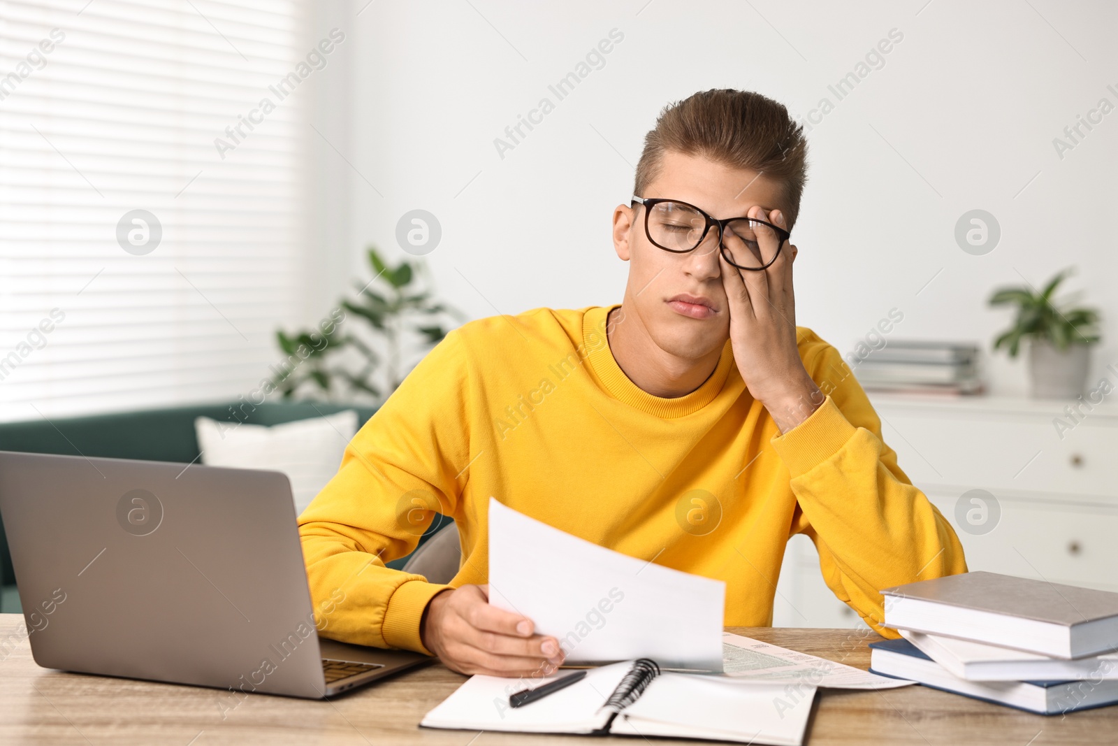 Photo of Tired student preparing for exam at table indoors