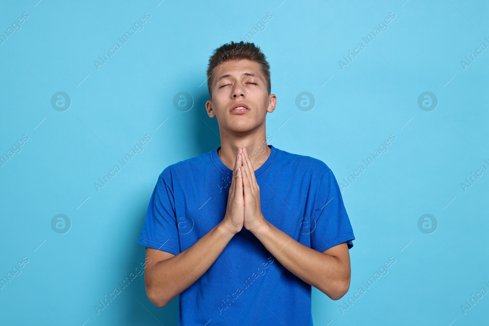 Photo of Student praying for good exam result on light blue background