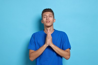 Photo of Student praying for good exam result on light blue background