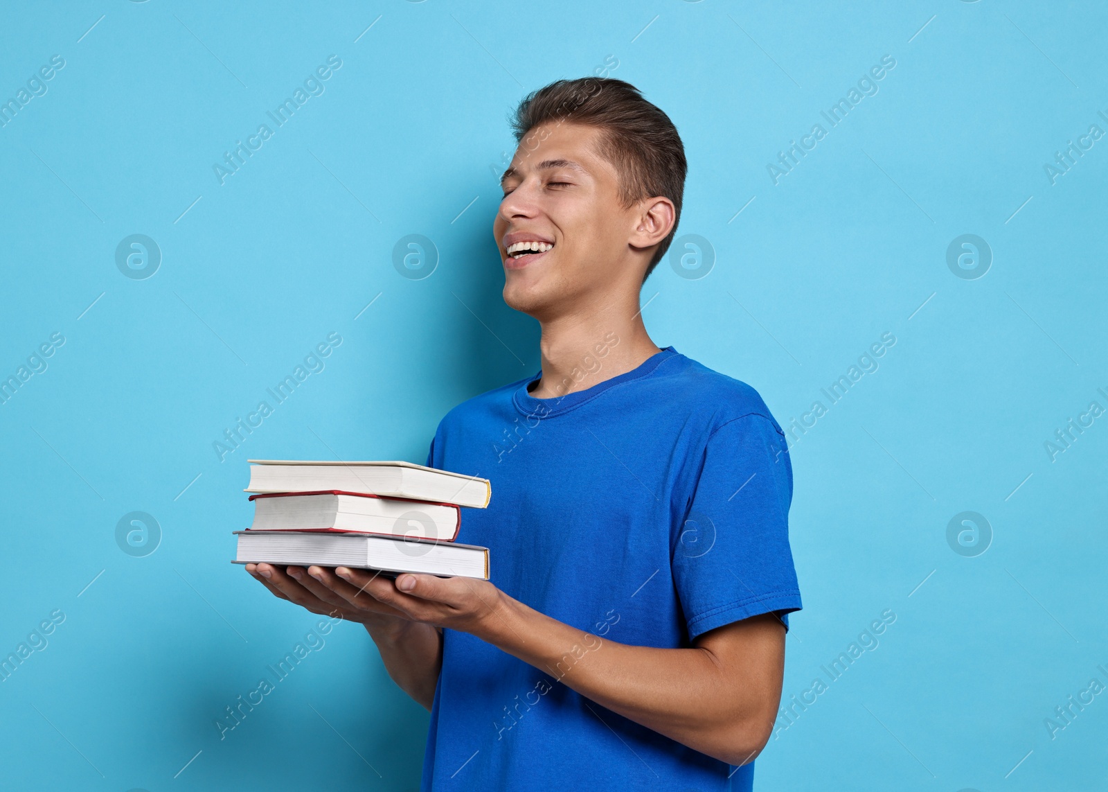 Photo of Happy student with stack of books on light blue background