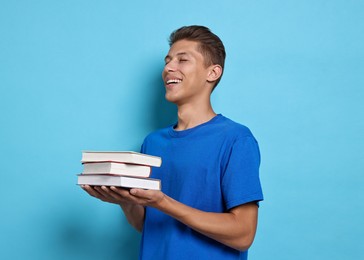 Happy student with stack of books on light blue background