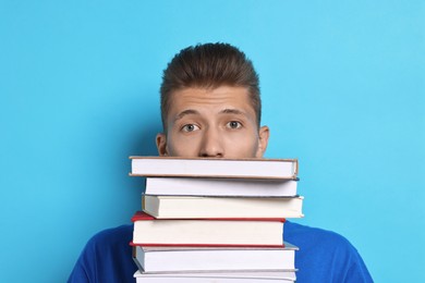 Photo of Tired student with stack of books having stress before exam on light blue background