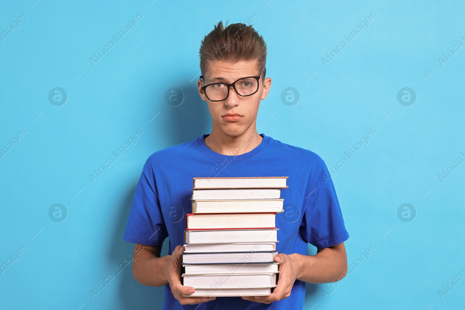 Photo of Tired student with stack of books having stress before exam on light blue background