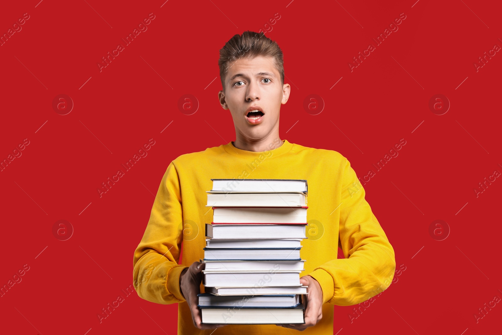 Photo of Emotional student with stack of books having stress before exam on red background