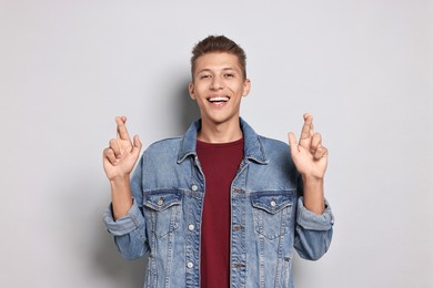 Photo of Emotional student with crossed fingers on grey background. Hope for good exam result