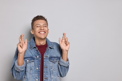 Photo of Emotional student with crossed fingers on grey background, space for text. Hope for good exam result