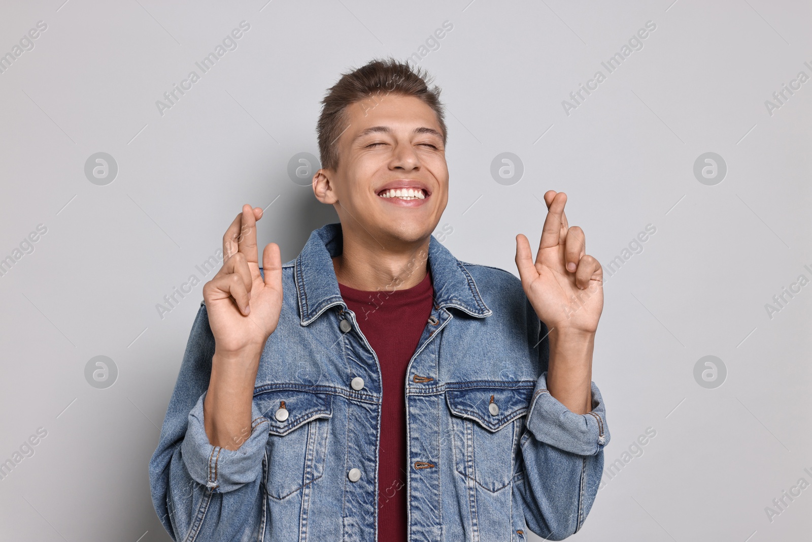 Photo of Emotional student with crossed fingers on grey background. Hope for good exam result