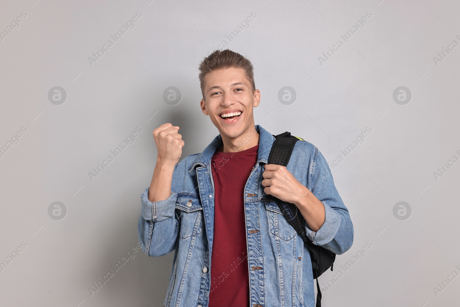 Photo of Student with backpack feeling happy about his good exam result on grey background