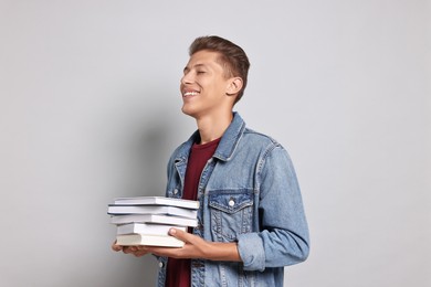 Photo of Happy student with stack of books on grey background