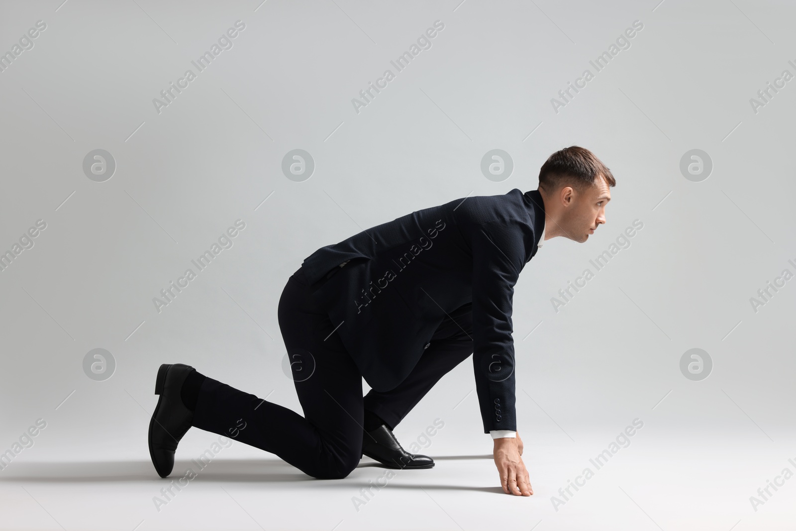 Photo of Businessman in starting position for run on light grey background