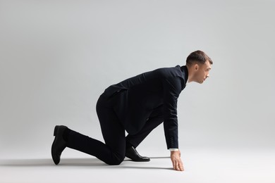 Businessman in starting position for run on light grey background