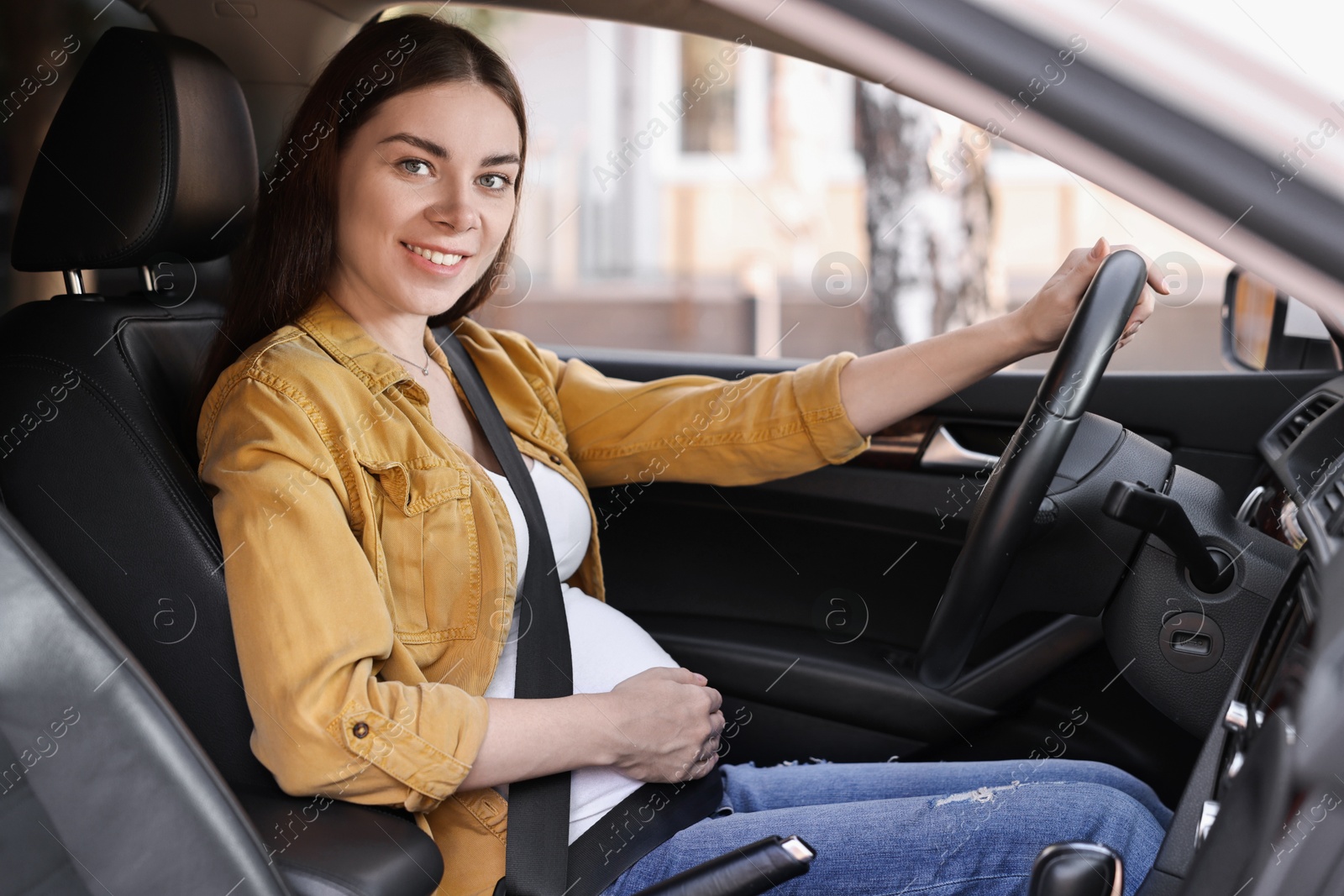 Photo of Smiling pregnant woman with safety belt driving car