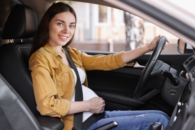 Photo of Smiling pregnant woman with safety belt driving car