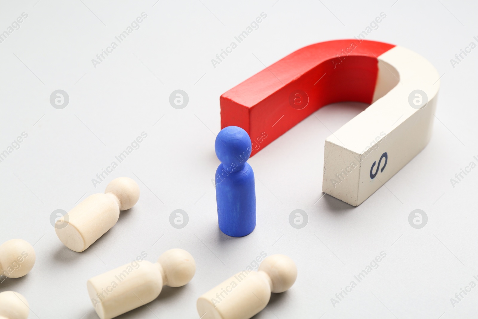 Photo of Magnet attracting human figures on light grey background, closeup