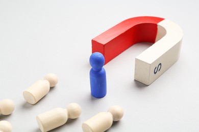 Photo of Magnet attracting human figures on light grey background, closeup