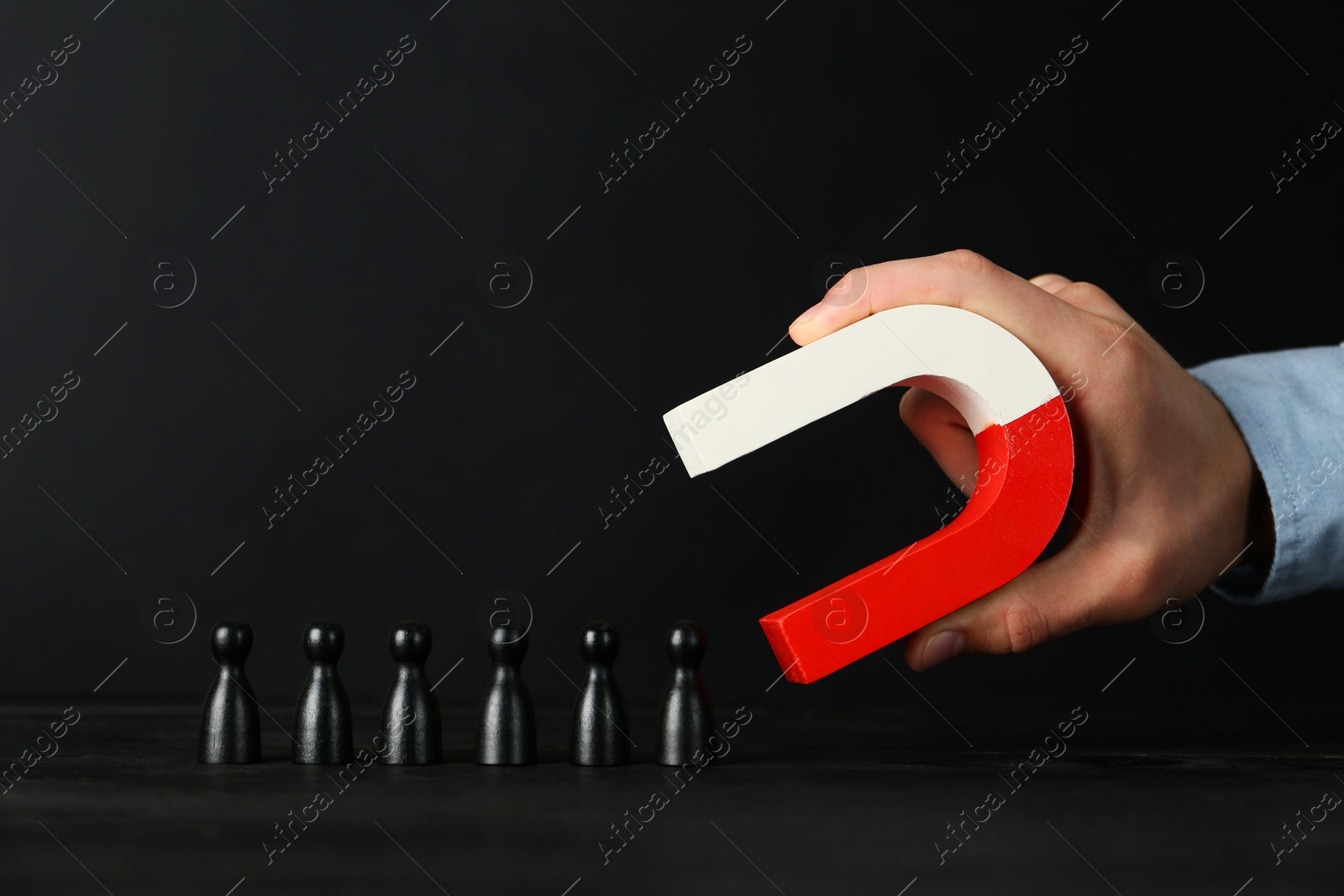 Photo of Man with magnet attracting black pieces at wooden table, closeup