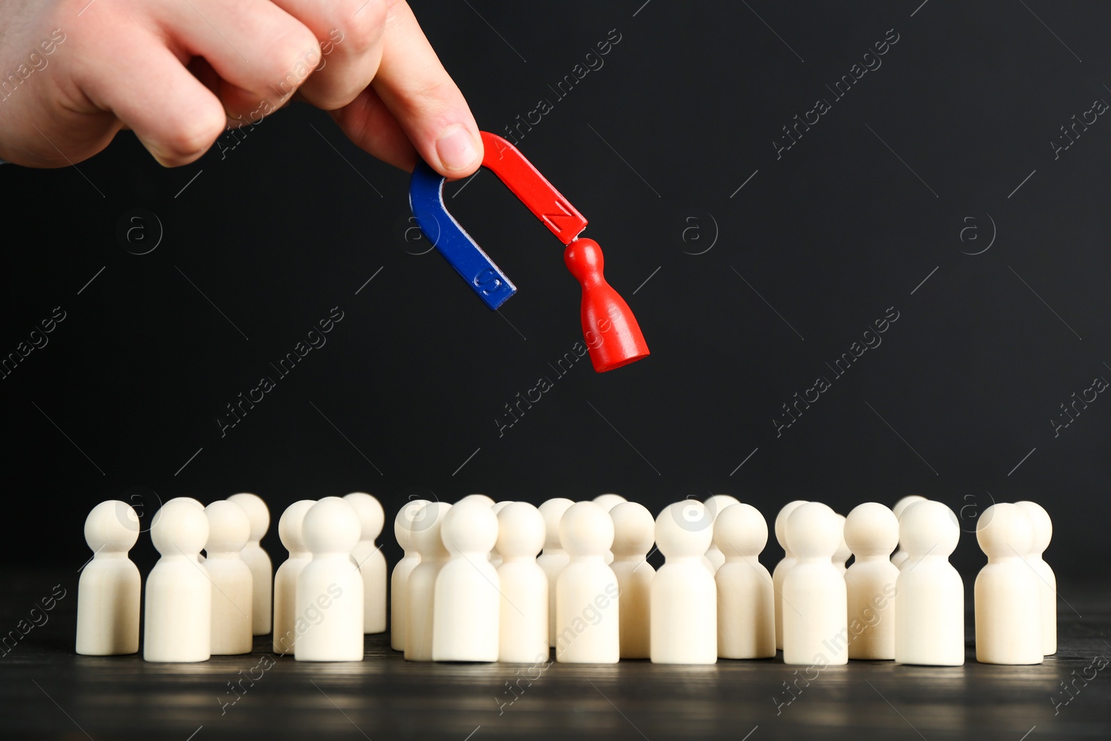 Photo of Man with magnet attracting red piece among wooden ones at black table, closeup