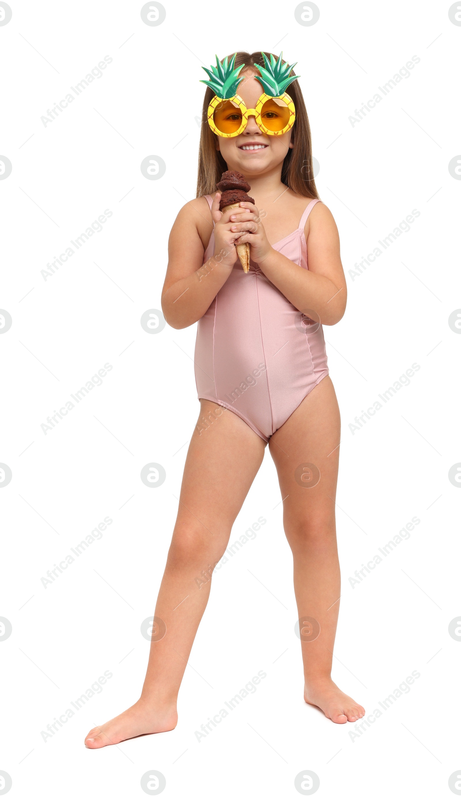 Photo of Cute little girl in swimsuit with funny sunglasses eating ice cream on white background