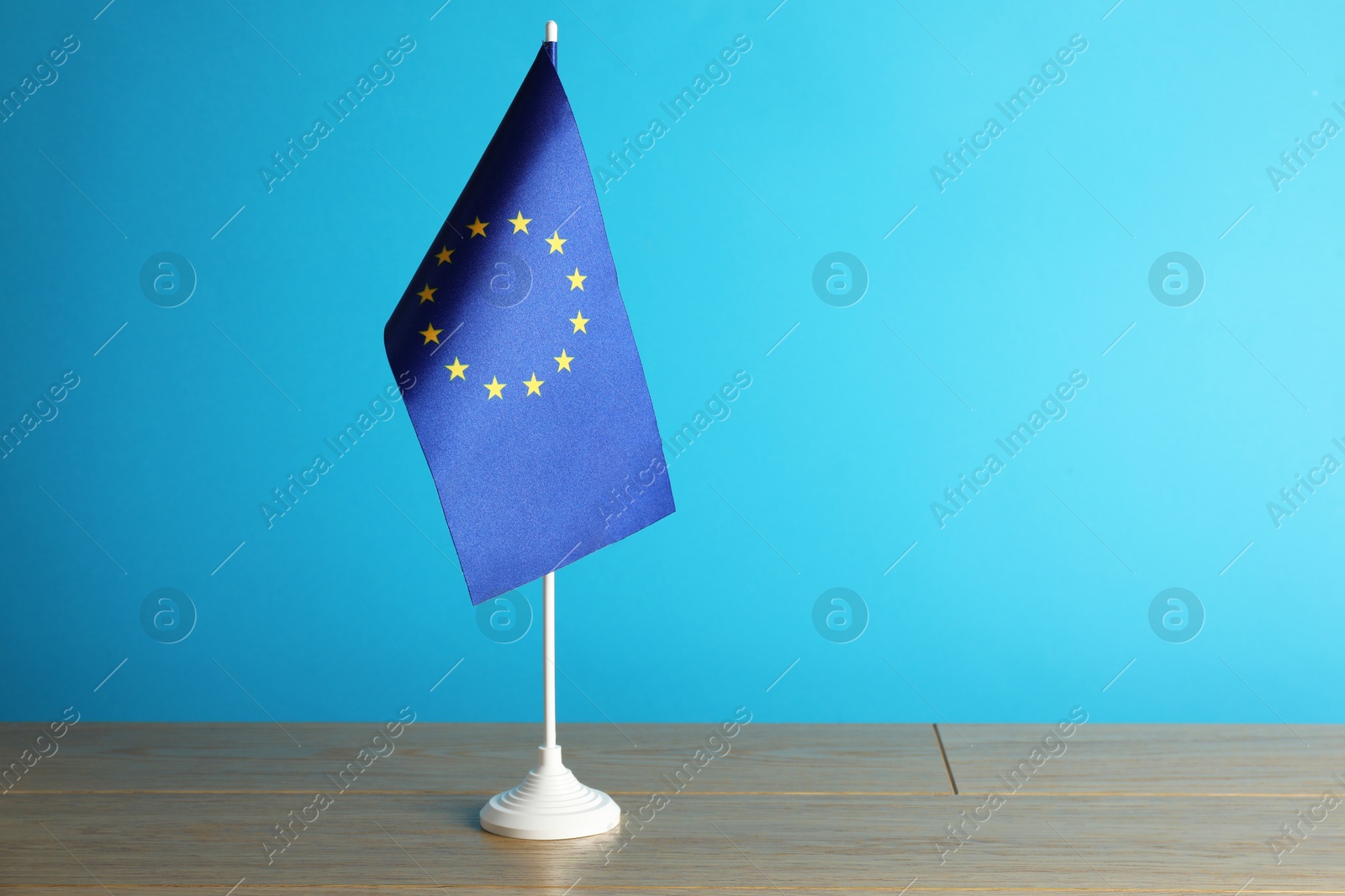 Photo of One flag of European Union on wooden table against light blue background. Space for text