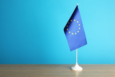 Photo of One flag of European Union on wooden table against light blue background. Space for text