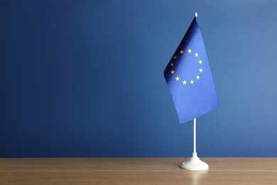 Photo of One flag of European Union on wooden table against blue background. Space for text