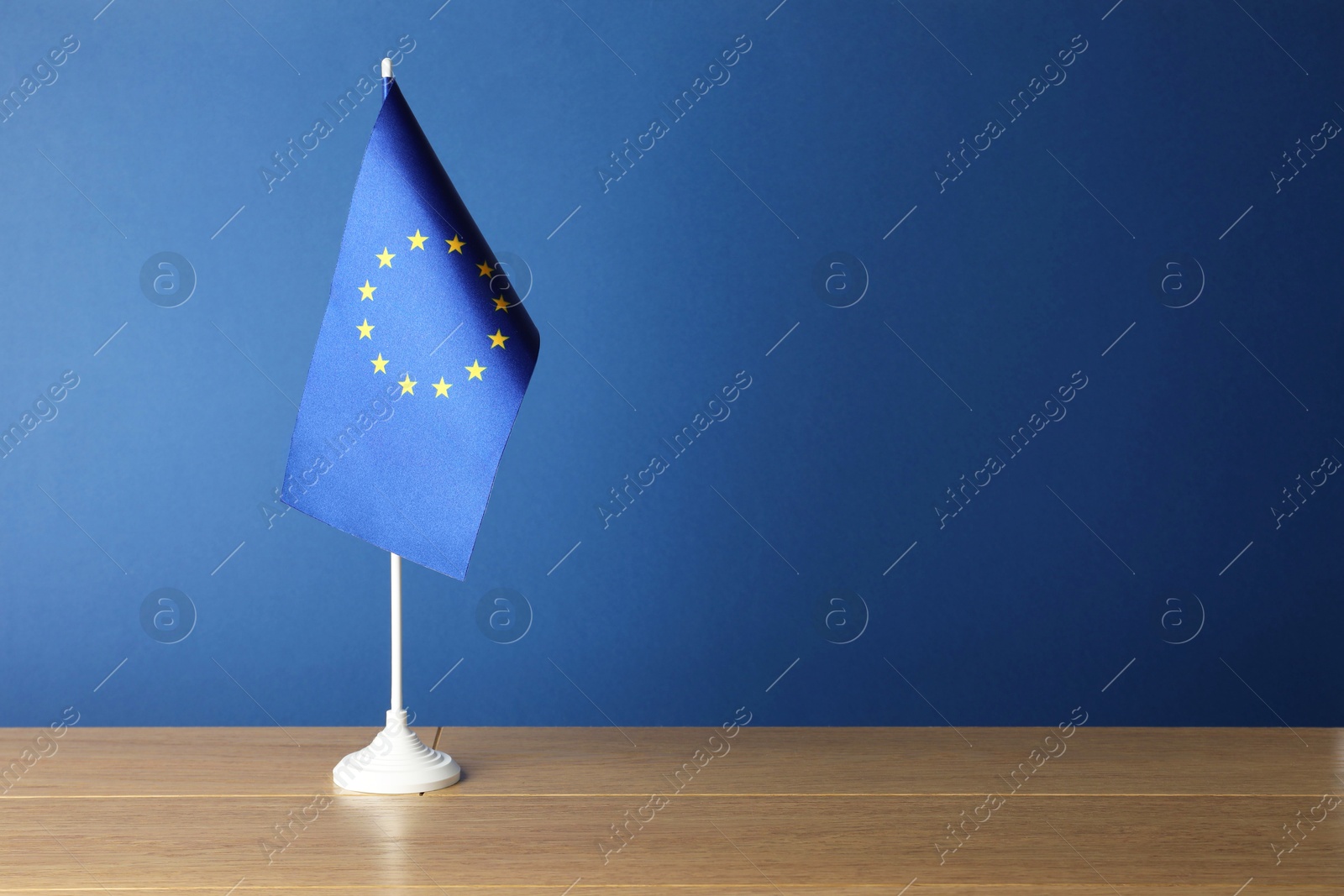 Photo of One flag of European Union on wooden table against blue background. Space for text